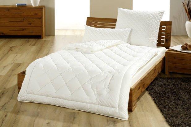 Weißes Kamelhaar-Steppbett auf Holzrahmenbett mit passenden Kissen in modernem Schlafzimmer